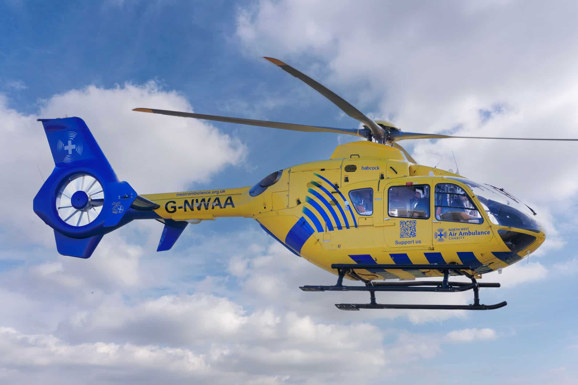 A yellow air ambulance helicopter flying against a backdrop of blue sky and clouds.