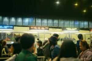 Crowded airport check-in area with people queueing and visible flight information signs.