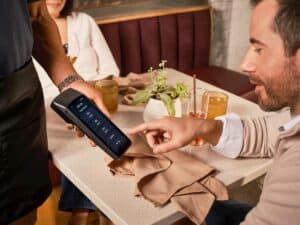 A diner uses a handheld POS system for digital tipping in a casual restaurant setting.