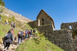 Visitors ascending the ancient stone steps of Machu Picchu, Peru, with clear blue skies and historic architecture.