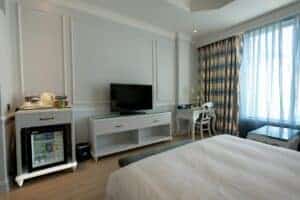 Bright and stylish hotel bedroom with TV, minibar, and cozy furnishings.