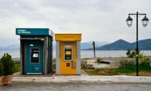 Outdoor ATMs by the Aegean coast in Greece with a scenic view of mountains and sea.