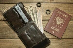 Brown leather wallet with cards, assorted currencies, and passport on wood surface.