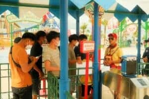 People in masks queue at an amusement park, reflecting new COVID-19 health protocols.