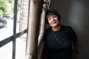 Portrait of a senior woman leaning by a window, bathed in natural light, looking thoughtful.