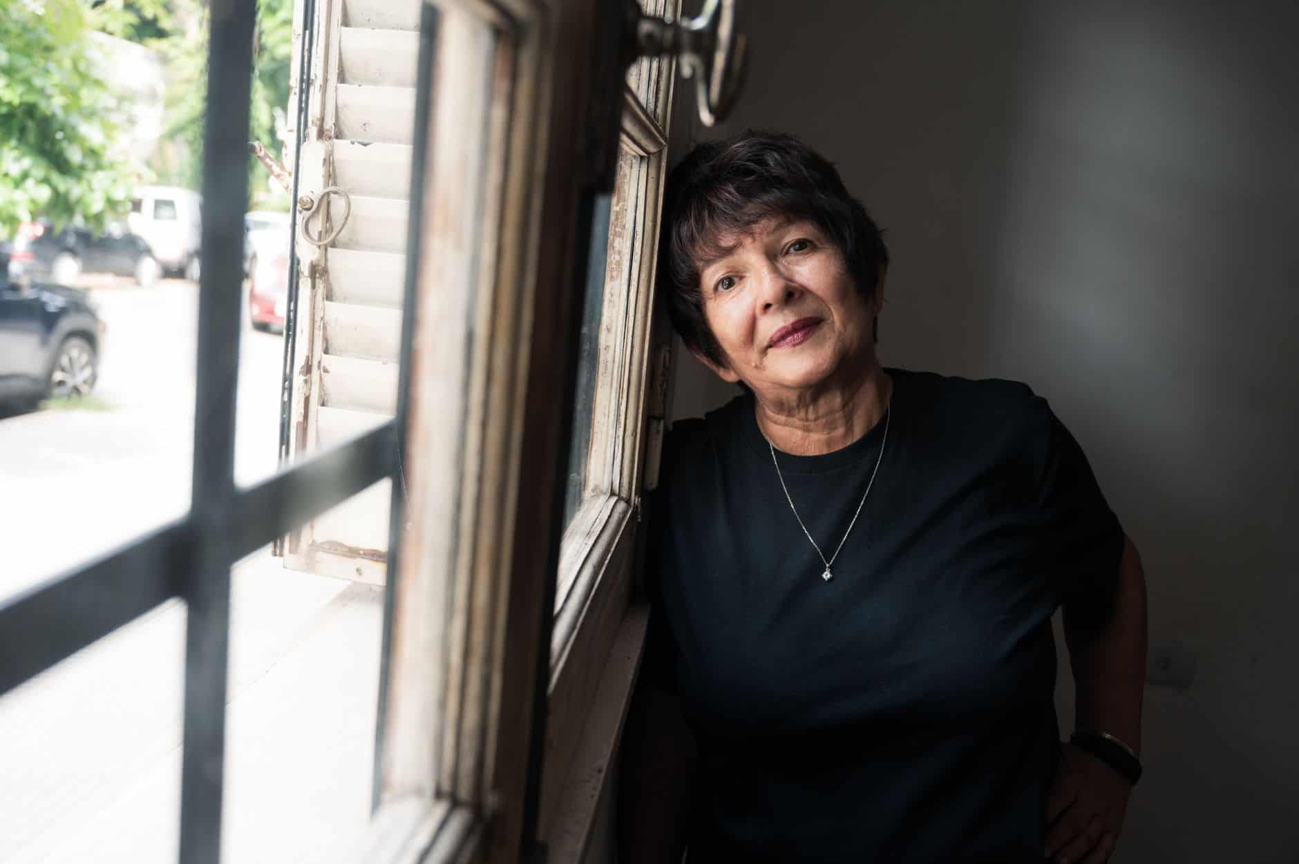 Portrait of a senior woman leaning by a window, bathed in natural light, looking thoughtful.