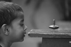 A curious child closely observes a spinning top with fascination.
