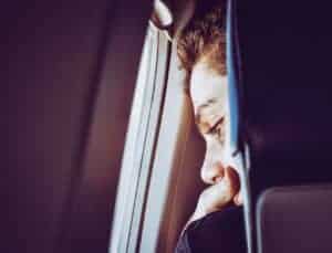 A young man looks thoughtfully out of an airplane window, captured in a close-up portrait.