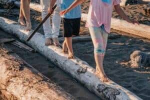 Children balancing on driftwood at the beach, enjoying playful outdoor adventure.