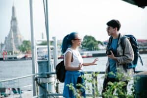 Travelers at Wat Arun, Bangkok, enjoy a conversation by the river. Perfect for travel themes.