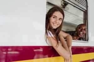Two women smiling out the train window, enjoying their travel adventure together.