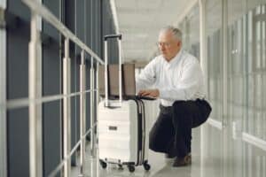 Full length of focused mature male in formal wear using laptop on baggage while having semisitting position in airport corridor