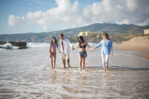 A joyful family strolls hand in hand along a scenic beach in Portugal, enjoying a sunny day.