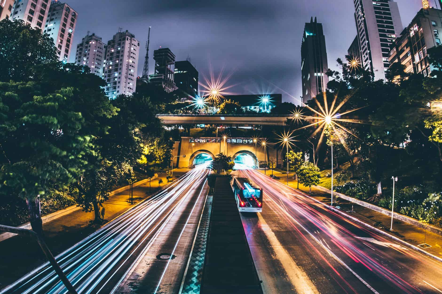 Captivating long exposure shot of a city highway at night, showcasing vibrant light trails and towering buildings.