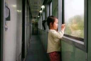 Asian girl with a camera looking out a train window, capturing reflective moment.