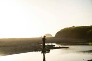 Silhouette of a man in black outfit standing on a coastal shore during sunset, capturing the natural beauty.