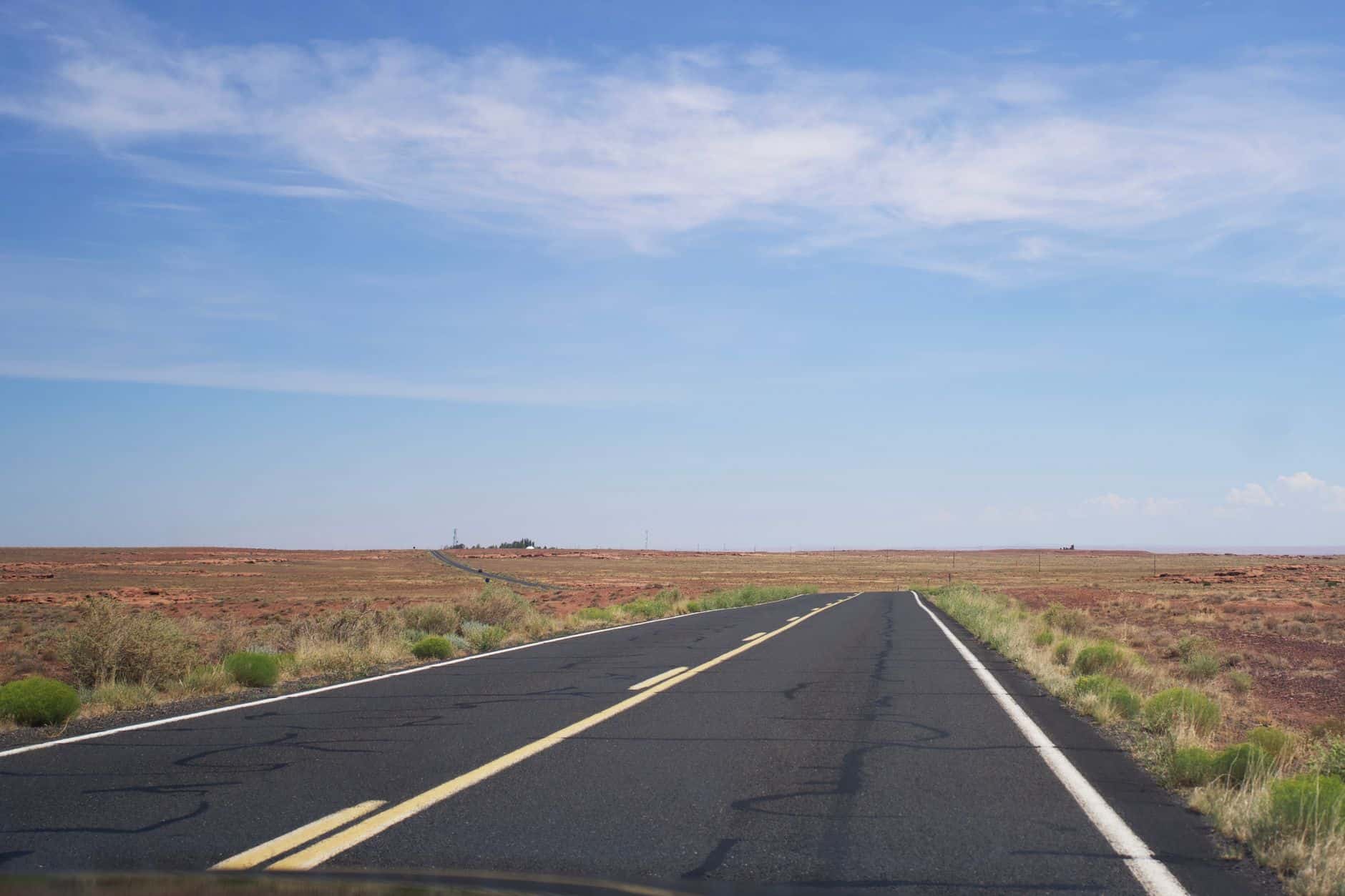 A long, empty road stretches into the desert landscape under a bright blue sky.