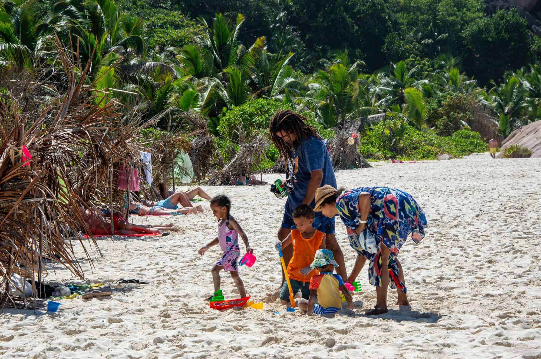 A family enjoys a day at a tropical beach, playing in the sand surrounded by palm trees under a bright summer sun.
