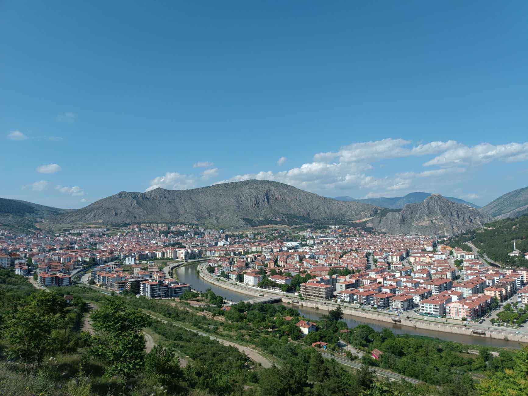 A panoramic view of a city nestled between lush greenery and rugged mountains under a clear blue sky.