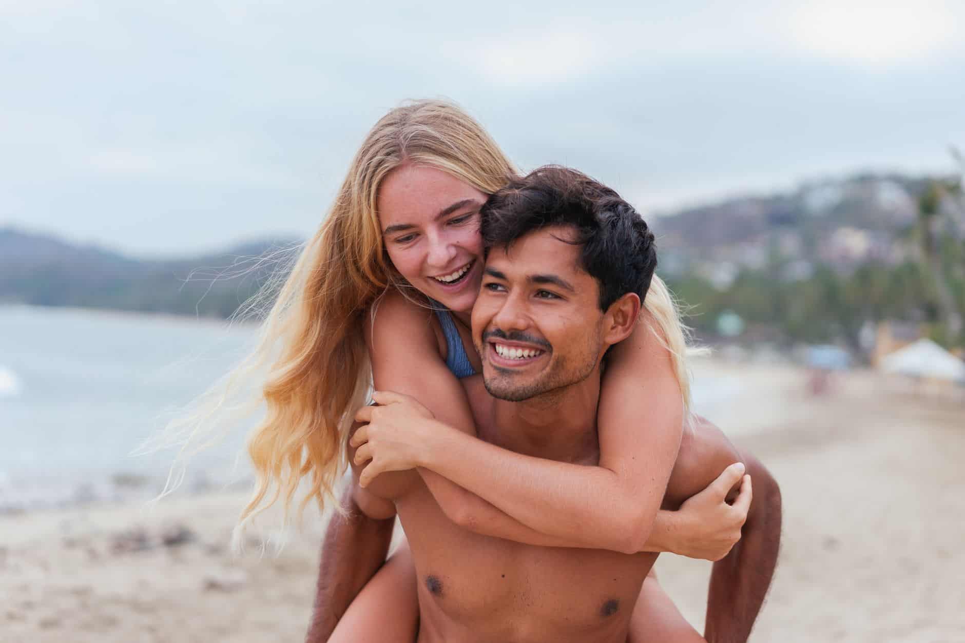Happy couple enjoying a playful piggyback ride on a scenic beach during sunset.