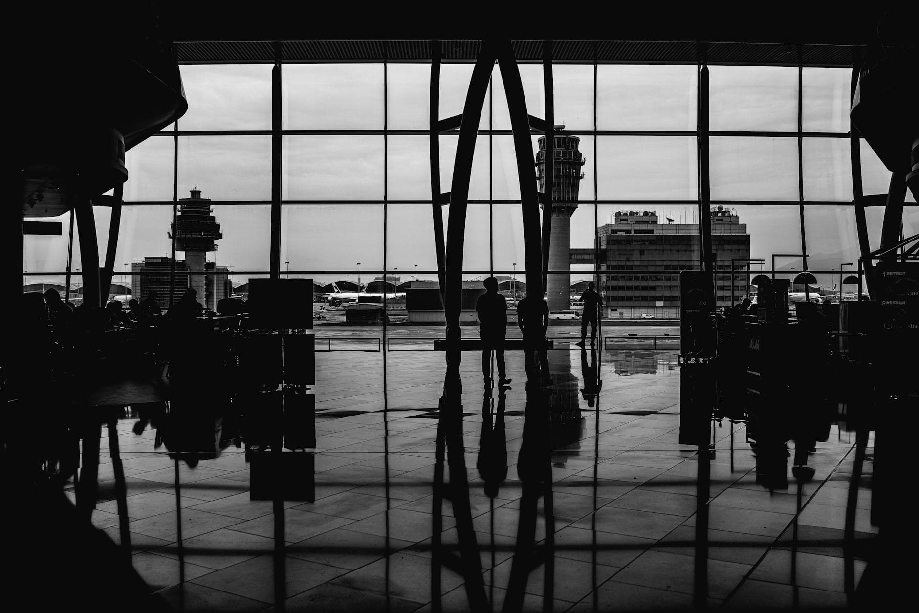 Black and white image of travelers silhouetted against large airport windows, capturing urban travel ambiance.