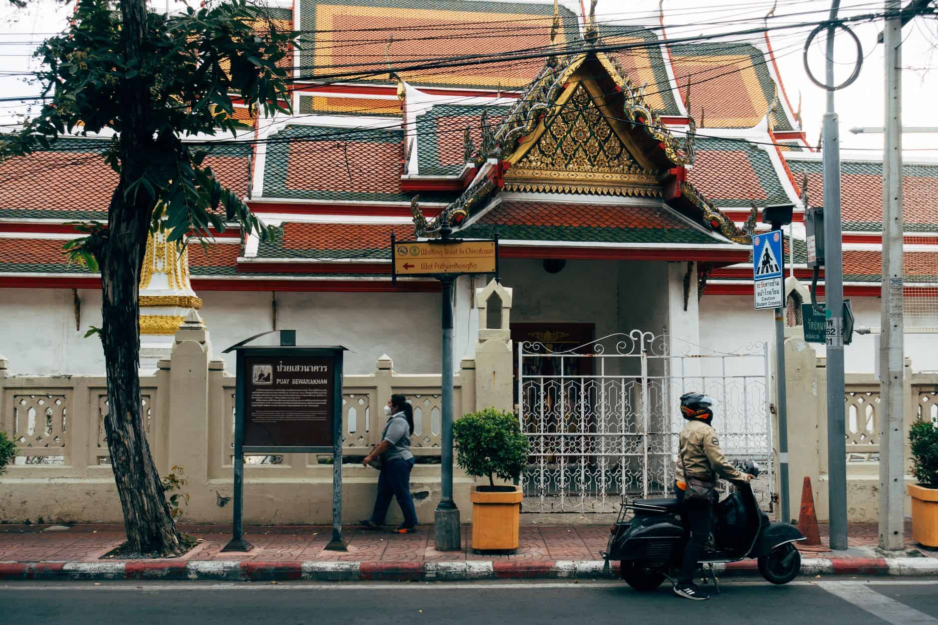 Motorcyclist and pedestrian in front of a Bangkok temple highlighting urban Thai culture.