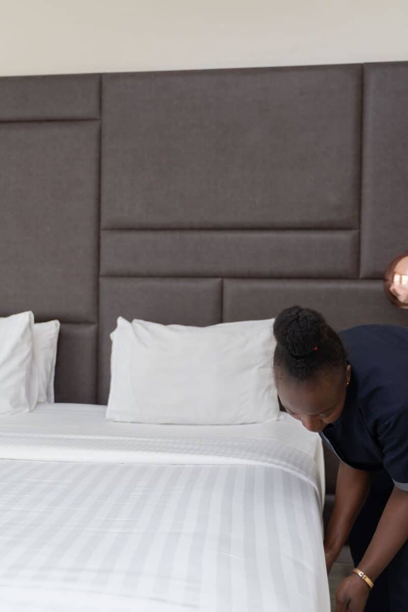 A hotel staff member prepares a bed in a sleek, modern hotel room with copper accents.