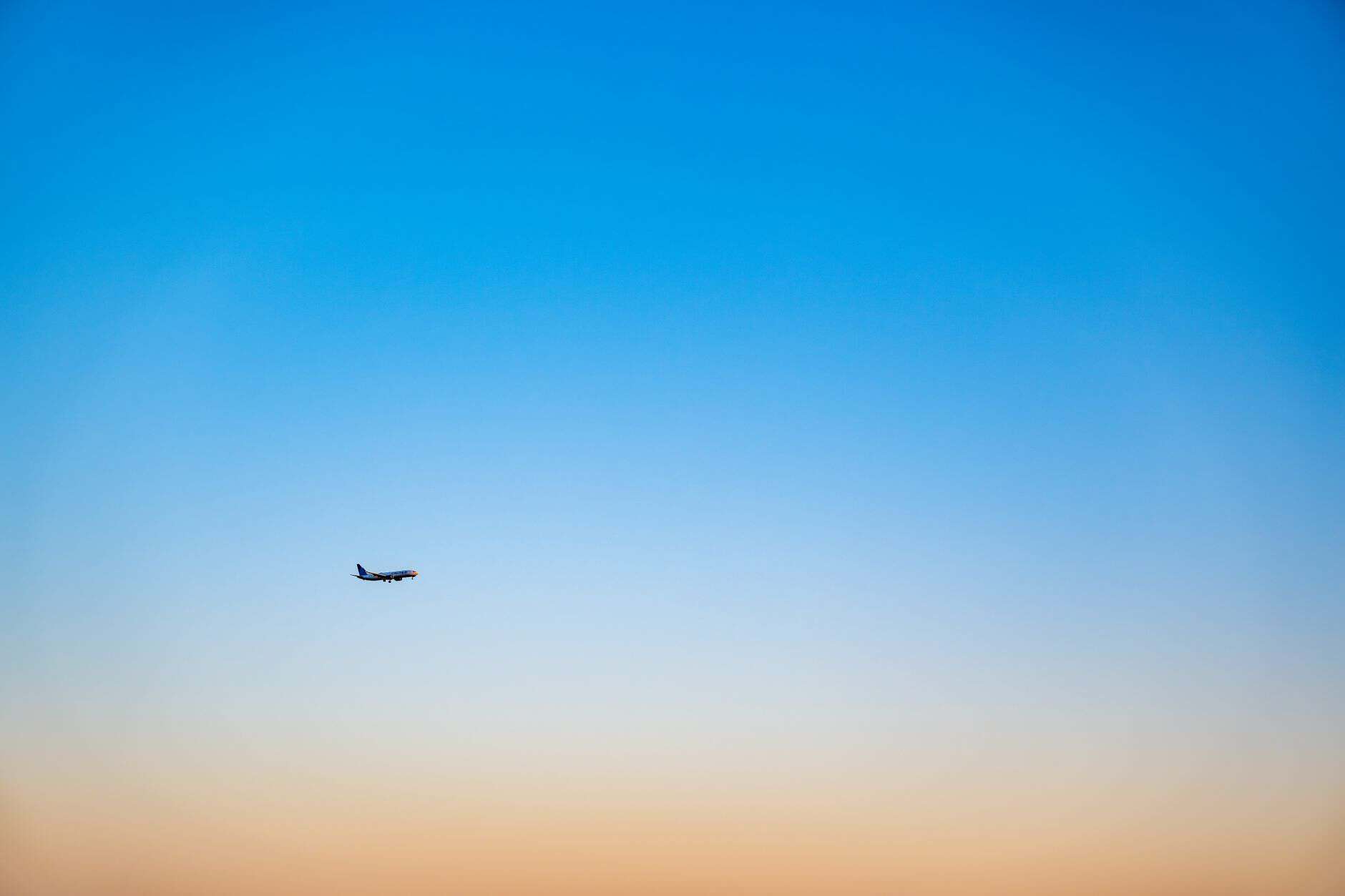 A lone airplane flying in a gradient blue and orange sky during sunset, creating a serene travel backdrop.