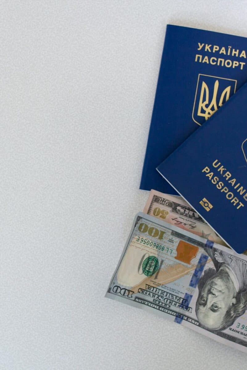 Top view of two Ukrainian passports with US dollar bills on a white surface.