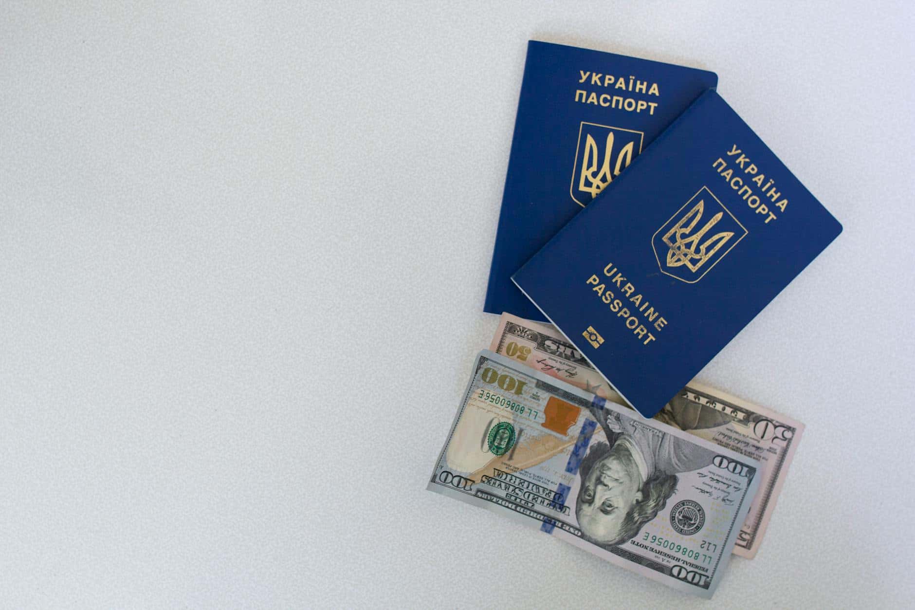Top view of two Ukrainian passports with US dollar bills on a white surface.