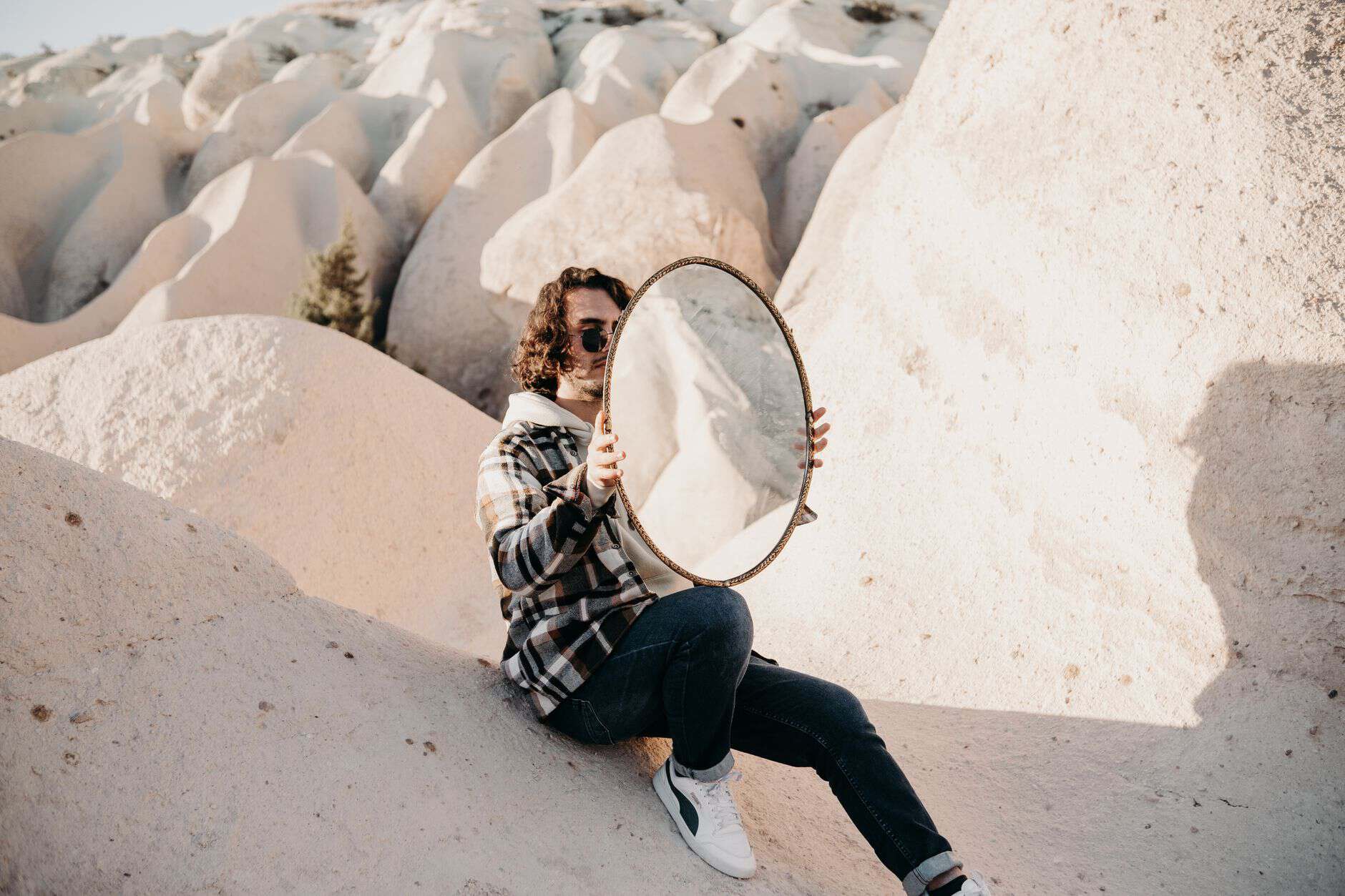 A person in a plaid jacket holding a mirror in a unique rocky desert landscape.