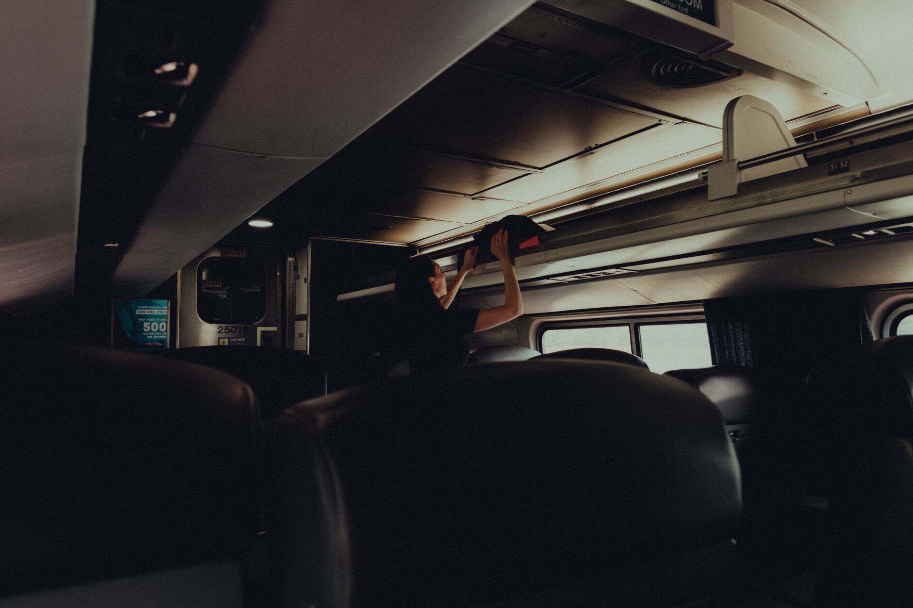 A woman placing her bag in the overhead rack on a modern train.