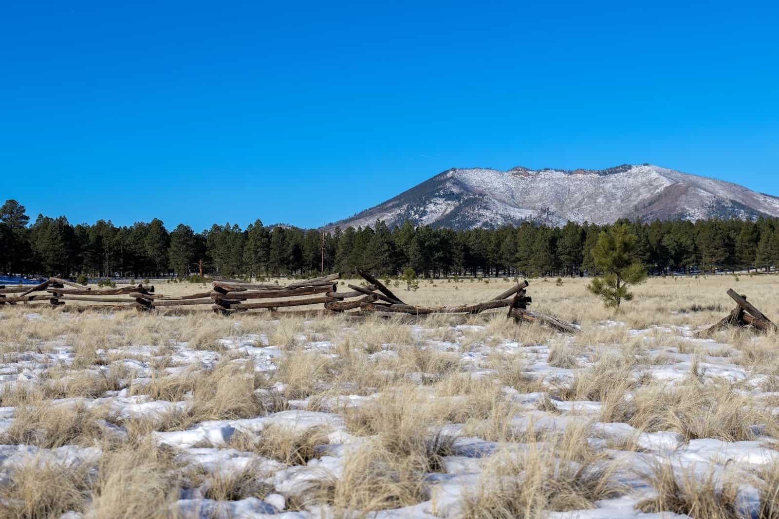 Tranquil view of snow-dusted Kendrick Peak with a rustic wooden fence in Arizona's serene landscape.