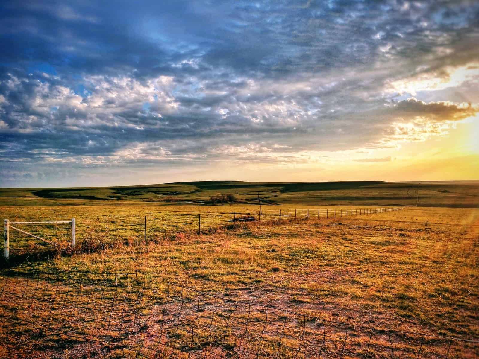Captivating sunrise over rural Kansas landscape with grassy fields and dramatic clouds.