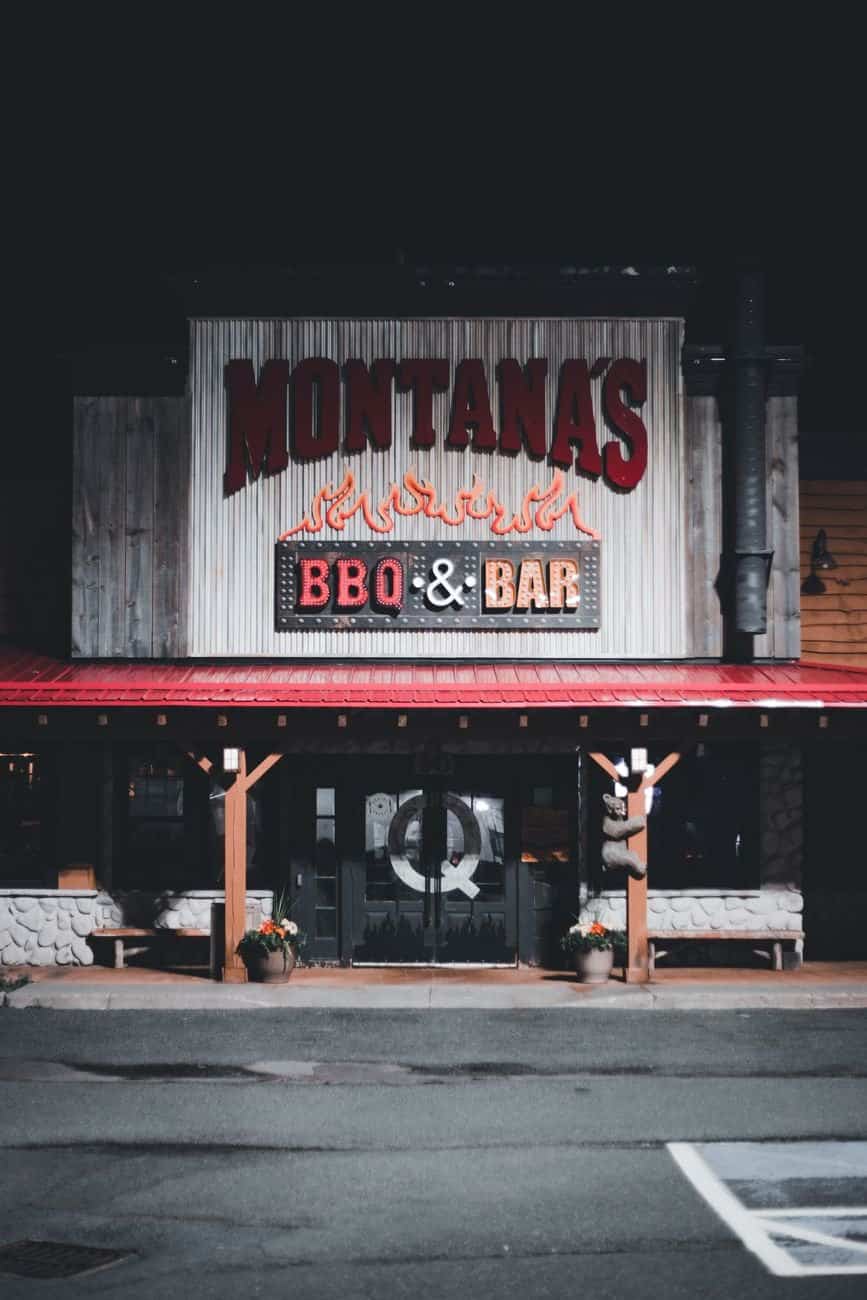 A rustic BBQ bar entrance illuminated at night with prominent signage.