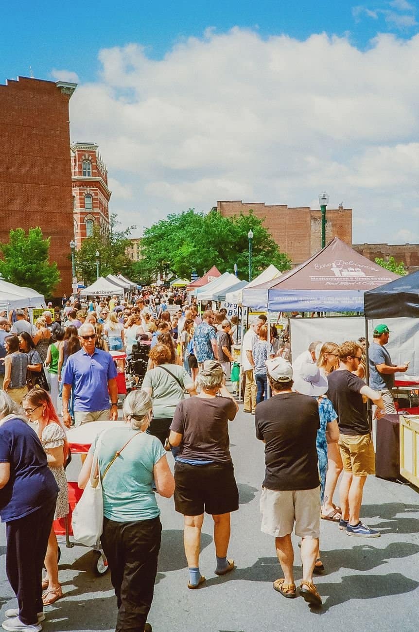 A bustling outdoor market with diverse people shopping under sunny skies.