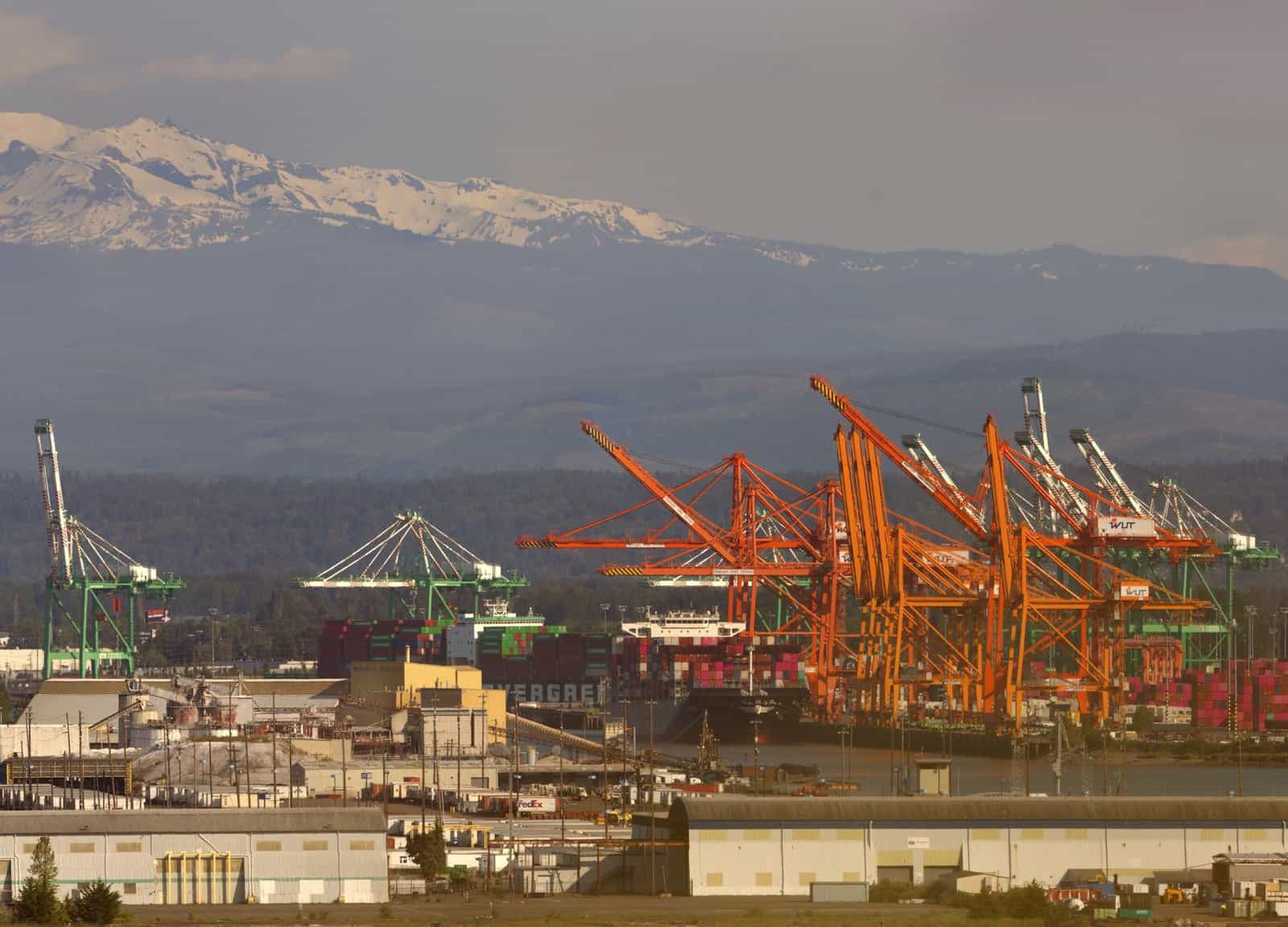 A vibrant scene of the Port of Tacoma with cranes and a mountainous backdrop, captured in daylight.