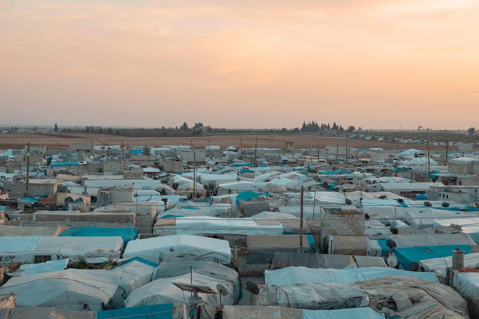 Aerial photo of a sprawling refugee camp under a vibrant sunset sky