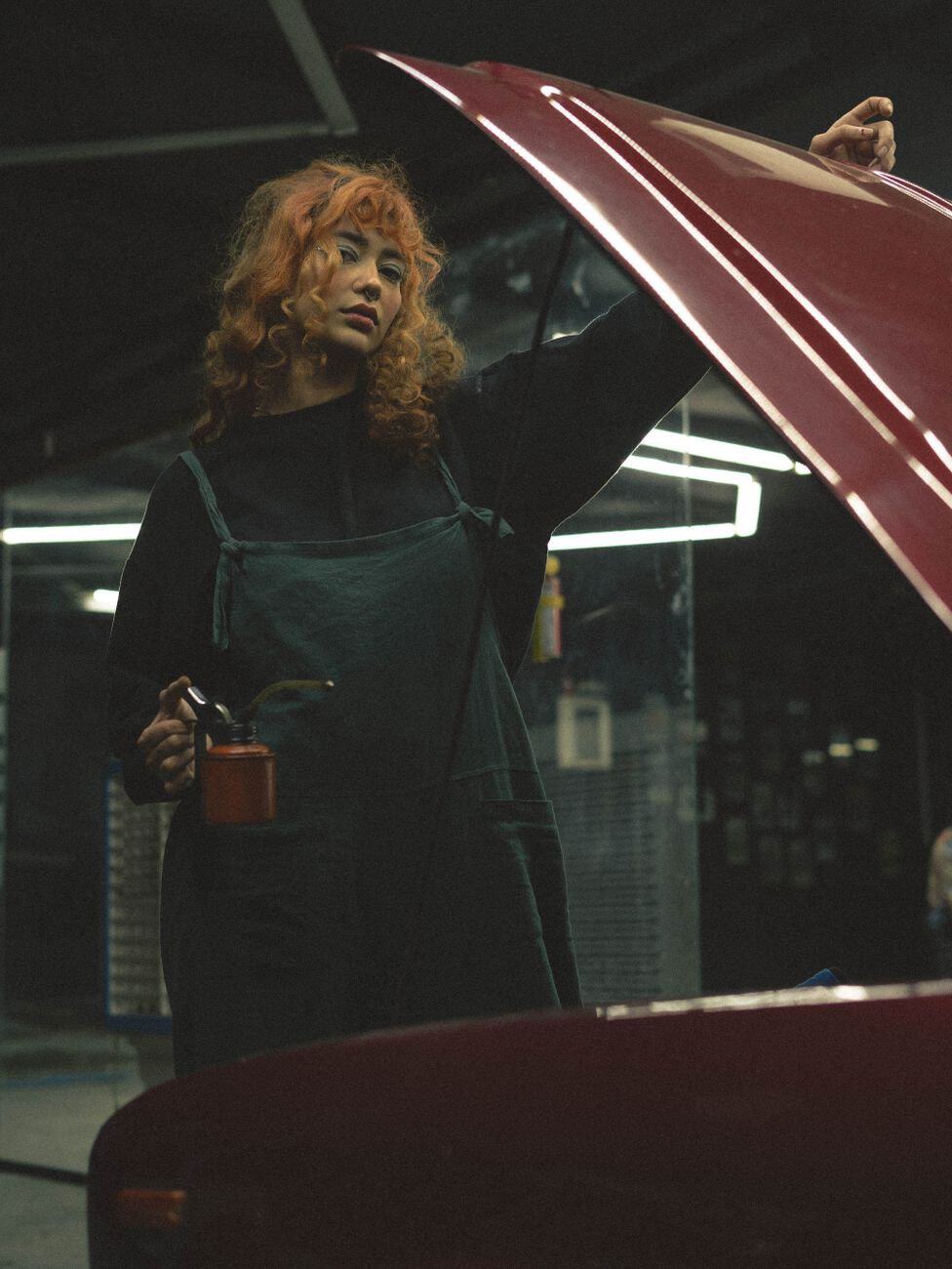 A woman mechanic with curly hair inspects a car engine in an indoor garage setting.