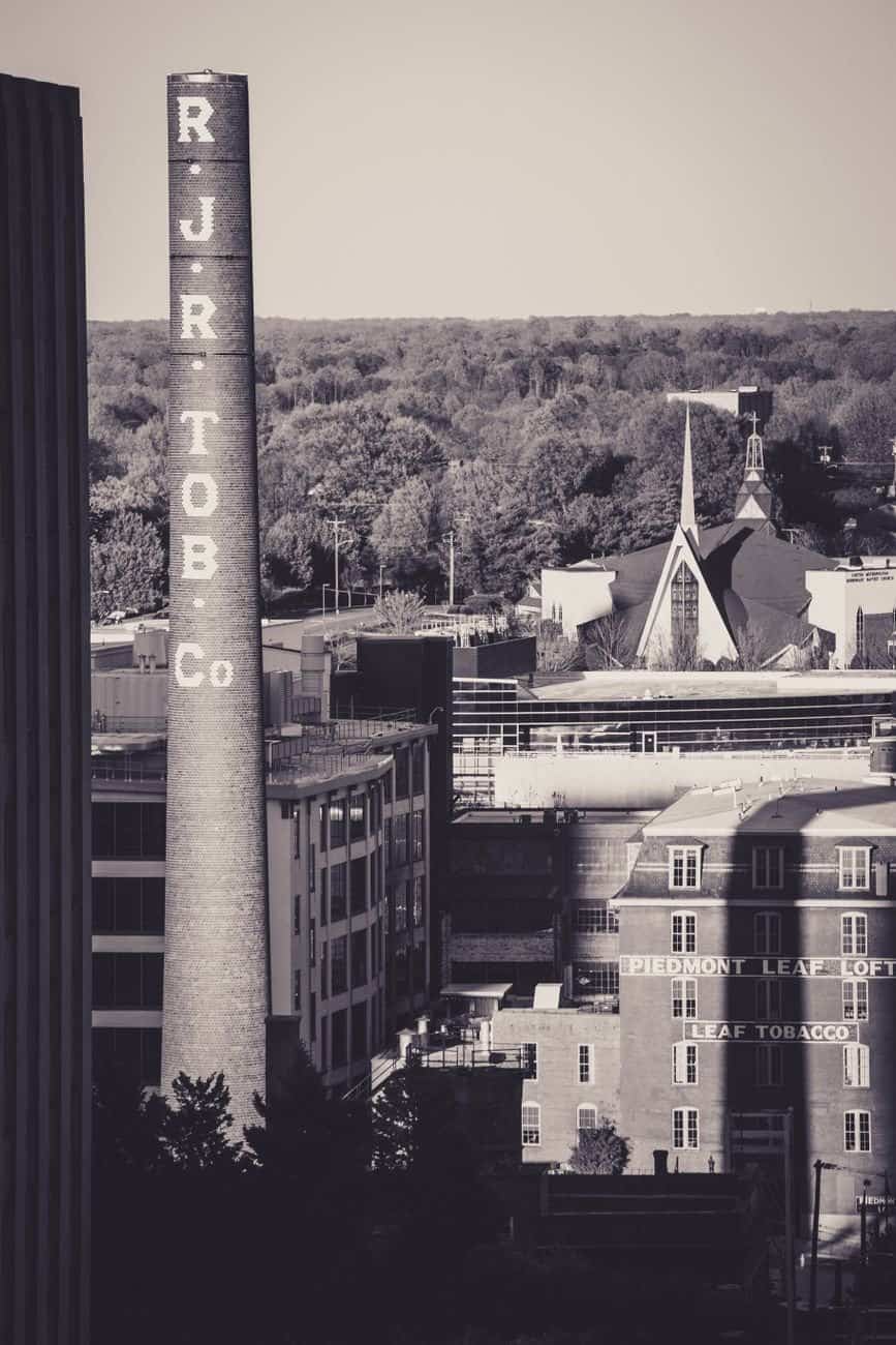 Vintage view of tobacco company buildings and smokestack in urban setting, highlights industrial heritage.