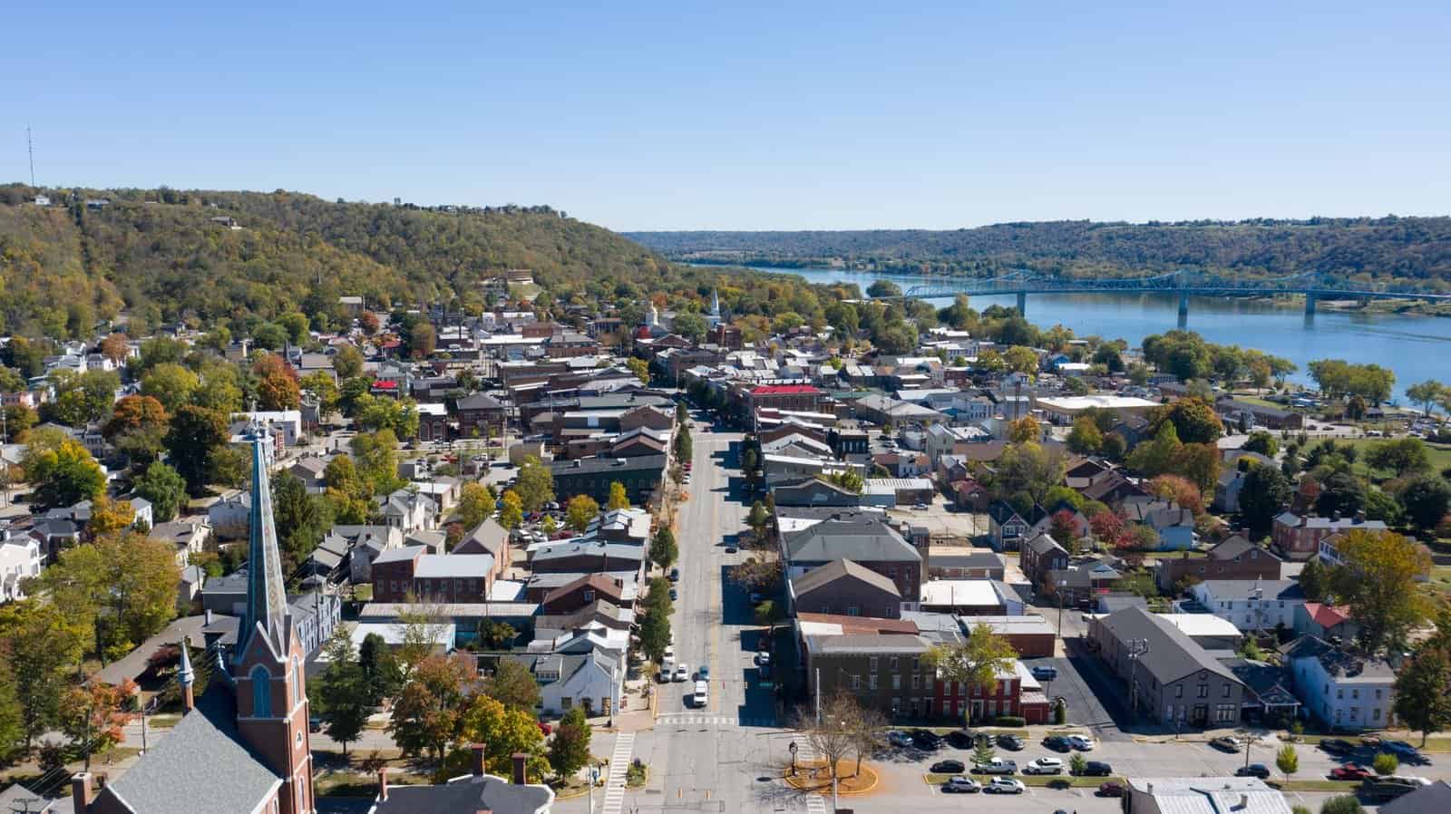 Scenic view of remote peaceful town located on shore of calm azure river beneath blue sky on clear summer weather