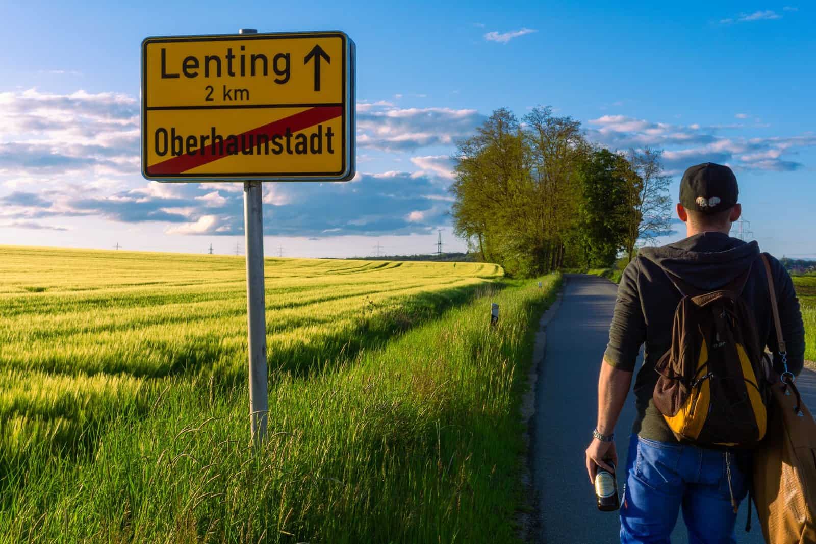 Man with backpack walking along a rural road near Lenting, Bavaria at sunset.