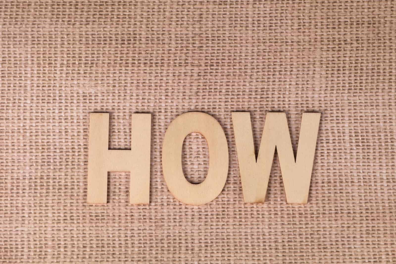 Word 'HOW' formed with wooden letters on textured burlap surface.