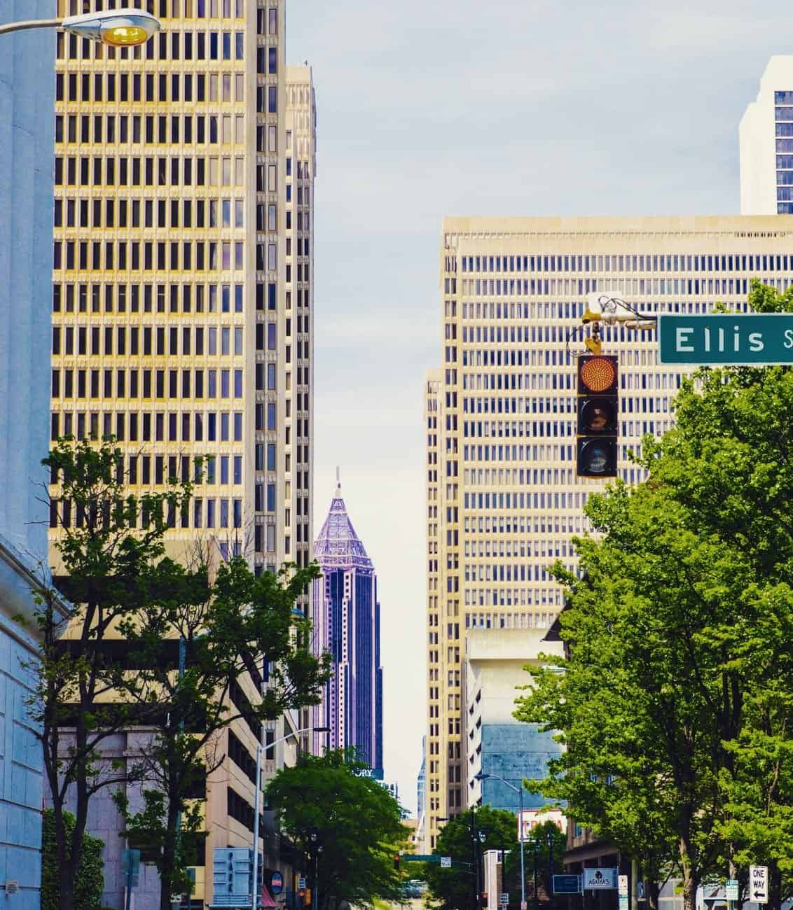 Urban streetscape view of Downtown Atlanta featuring skyscrapers, trees, and traffic lights.