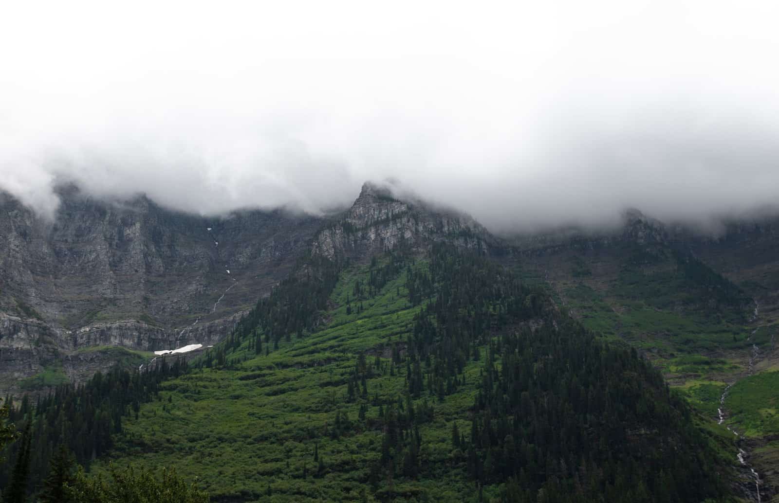 Scenic view of cloud-covered mountain peaks and lush greenery in Glacier National Park, MT.