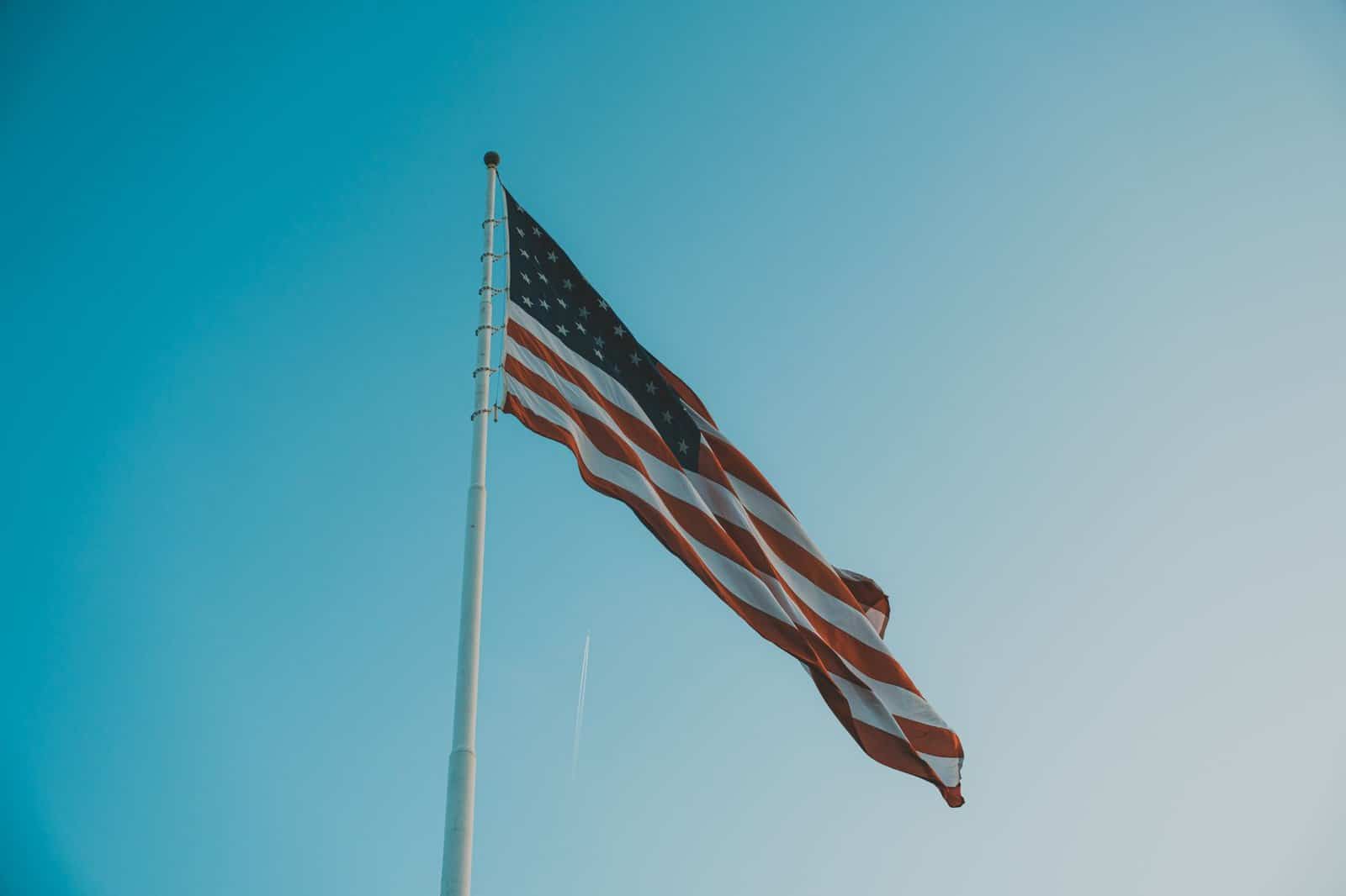 Low angle view of American flag waving on a flagpole against a bright clear sky.