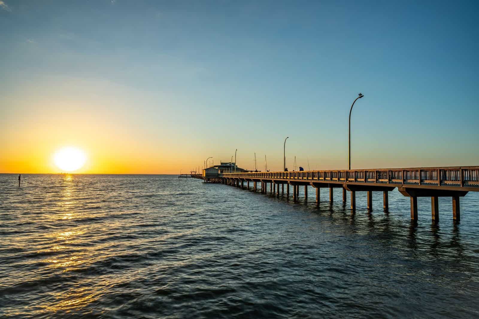Tranquil scene of a sunset over Fairhope Pier in Alabama with a clear sky and calm sea.