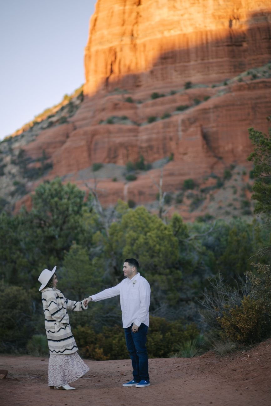 A couple holding hands in front of Sedona's iconic red rock formations, embracing nature.