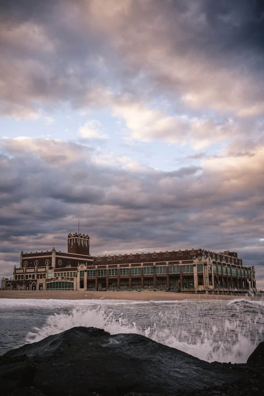 Dramatic ocean view of Asbury Park Convention Hall under cloudy sky.