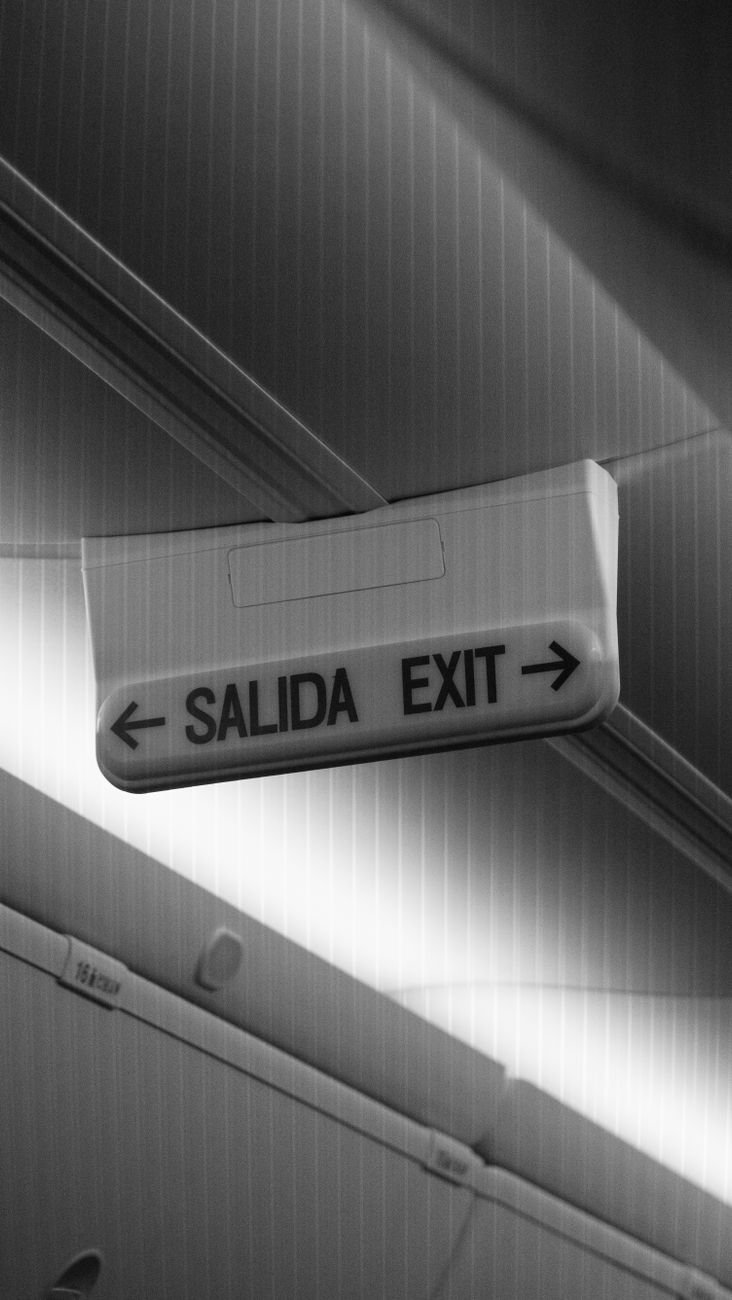 Black and white photo featuring a bilingual exit sign in an airplane cabin.